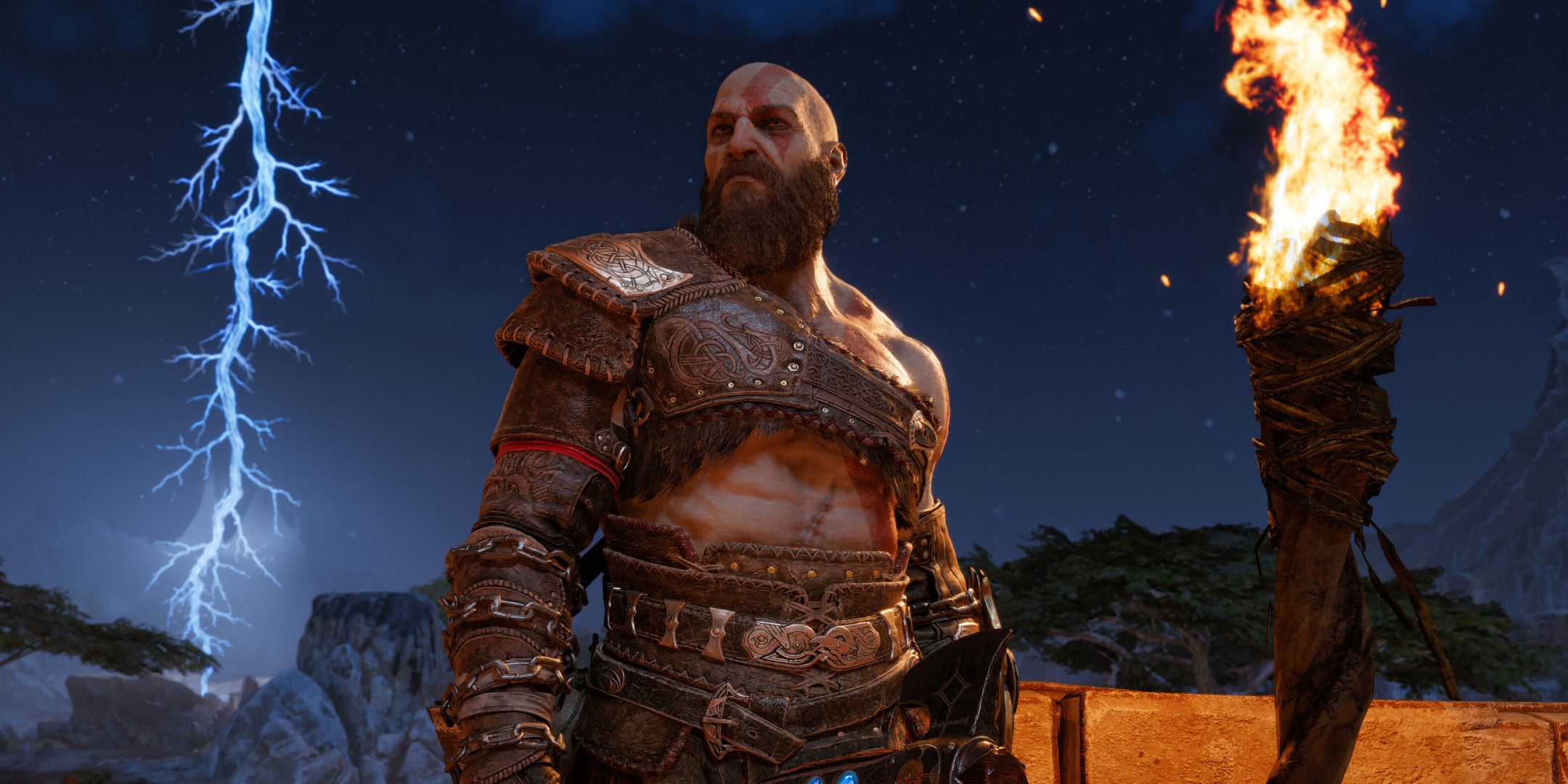 Kratos standing next to a torch during a lightning storm from God of War Ragnarok.