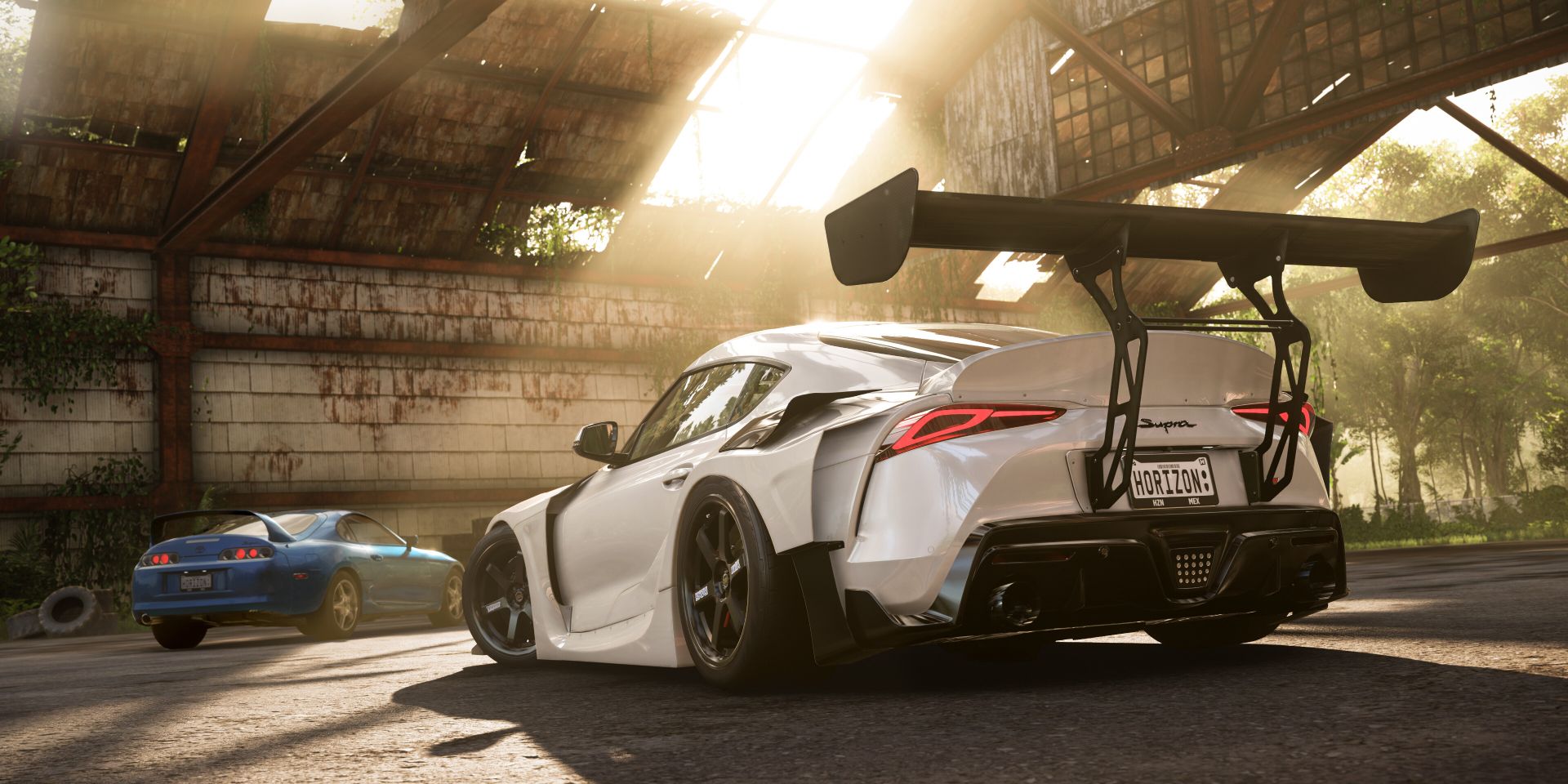 Forza Horizon 5 screenshot showing a white and blue supercars racing each other in an abandoned hangar.