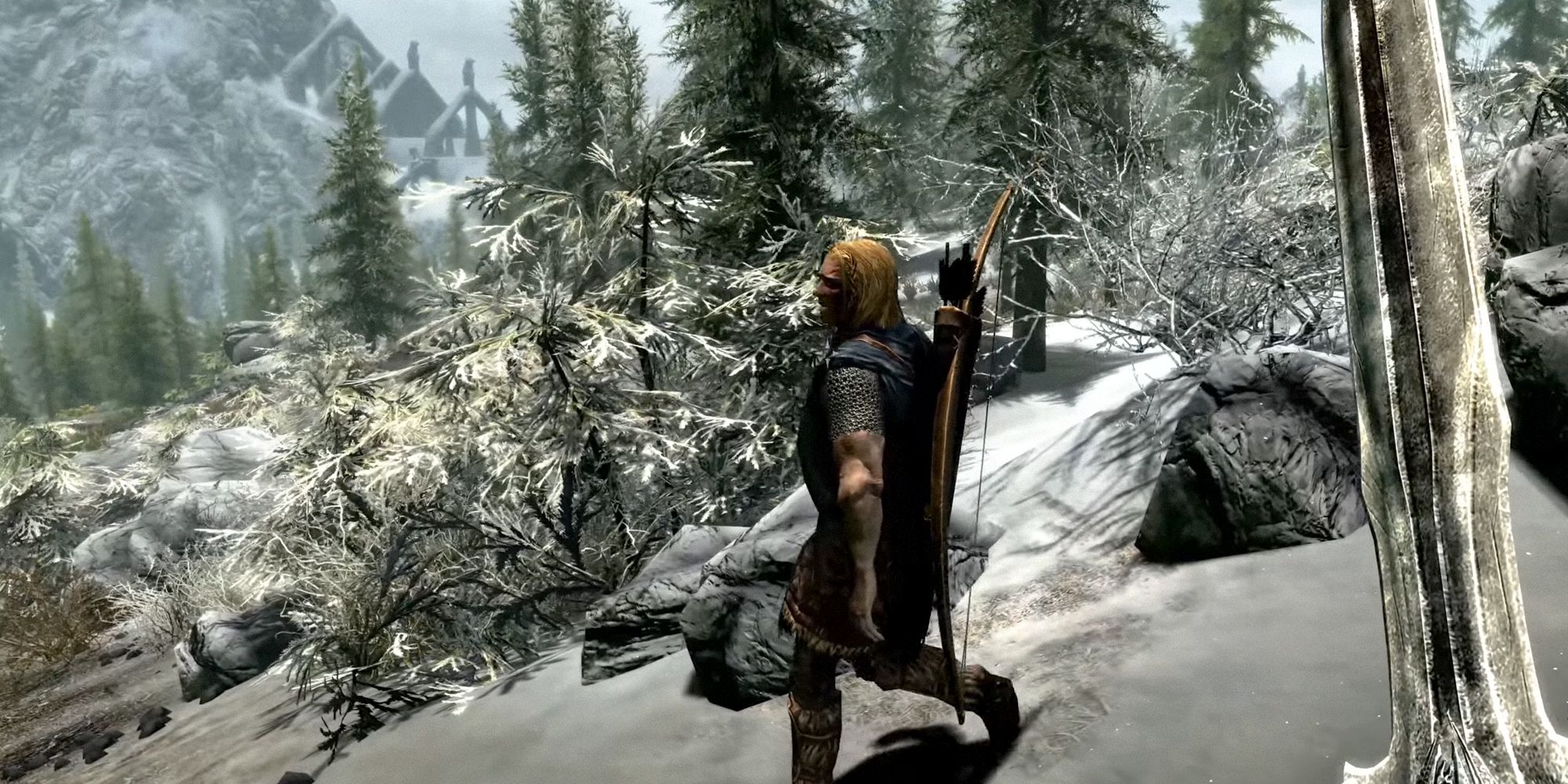 Skyrim protagonist wielding a sword while walking down a snowy hill. NPC to their right.