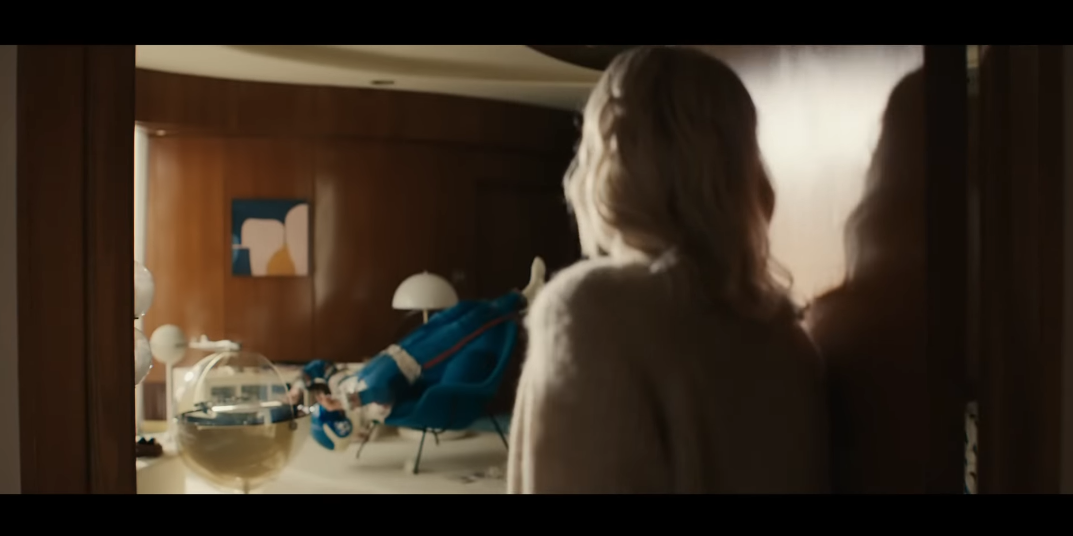 Blonde woman opens a door revealing a futuristic room with a blue suit, hinting at Fantastic Four's tech