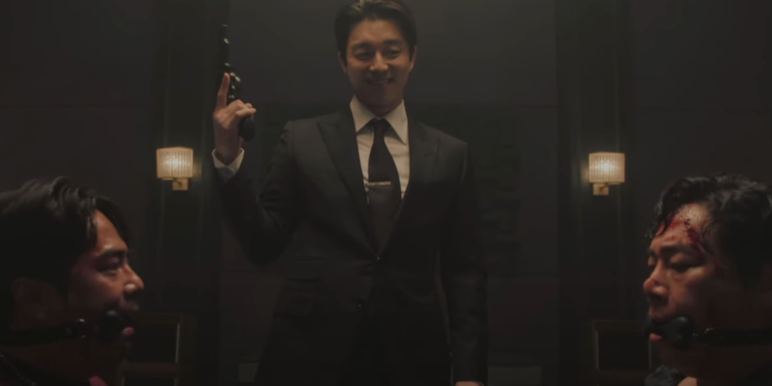 The Recruiter grins, wielding a gun before a restrained and scared Jeong-rae and Woo-seok. 