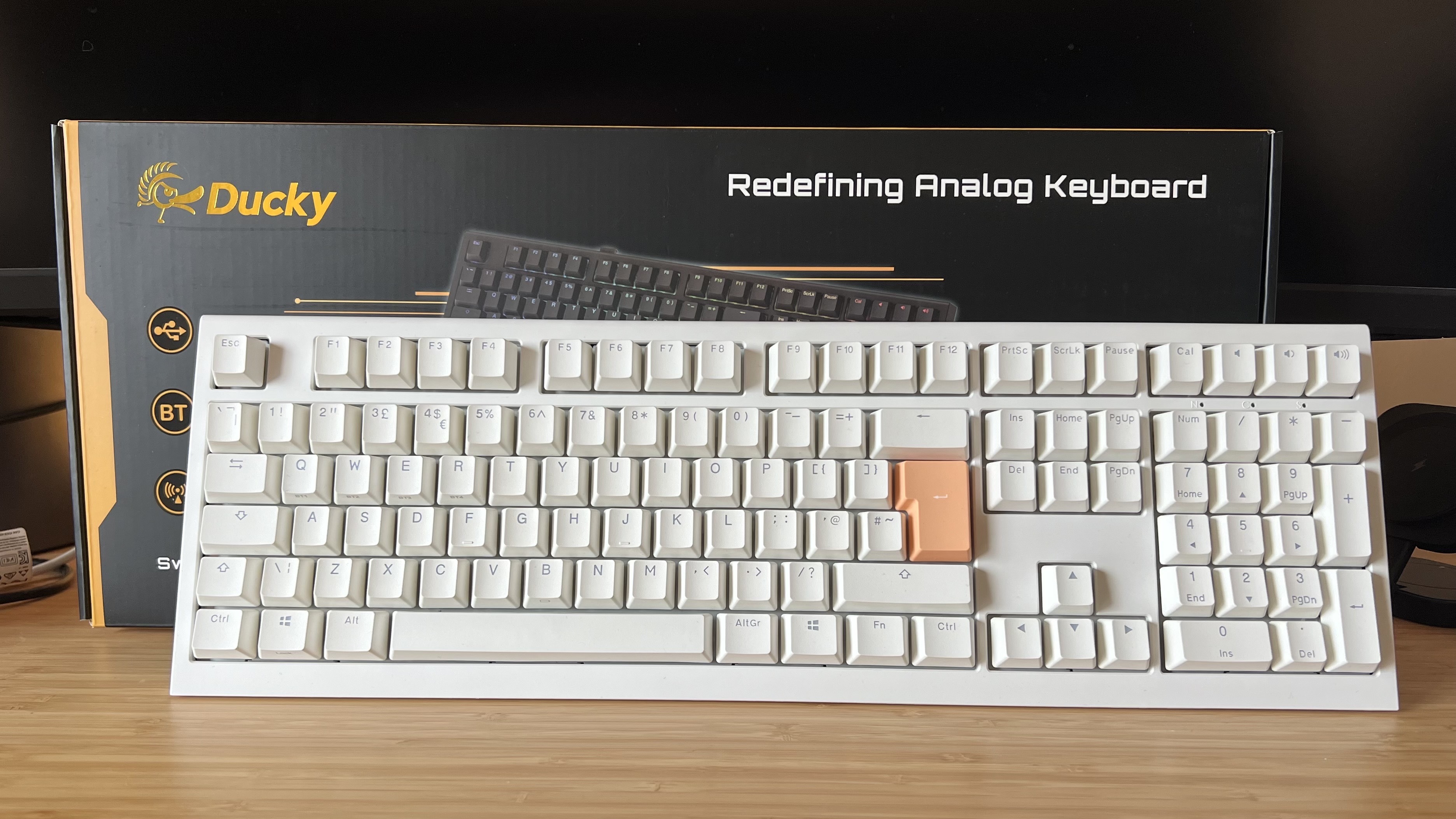 Ducky One X keyboard leaning against packaging on a wooden desk