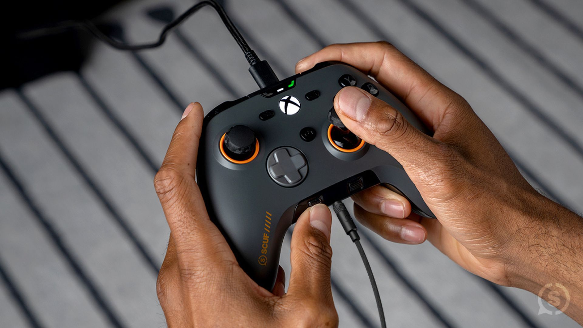 The Scuf Valor Pro being held in a marketing image with two wires connected to it