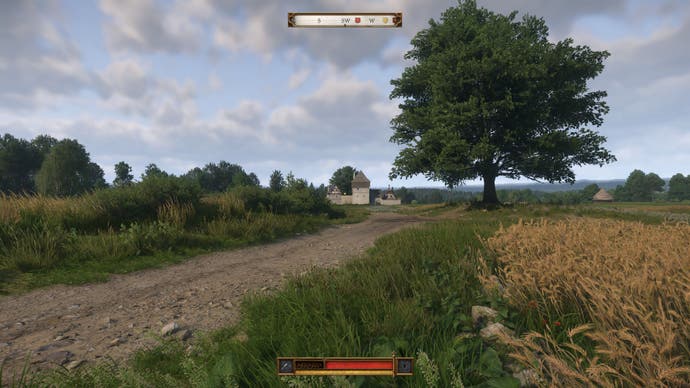 A small fortress appears in the distance as the player walks down a muddy track next to a wheat field in Kingdom Come Deliverance 2