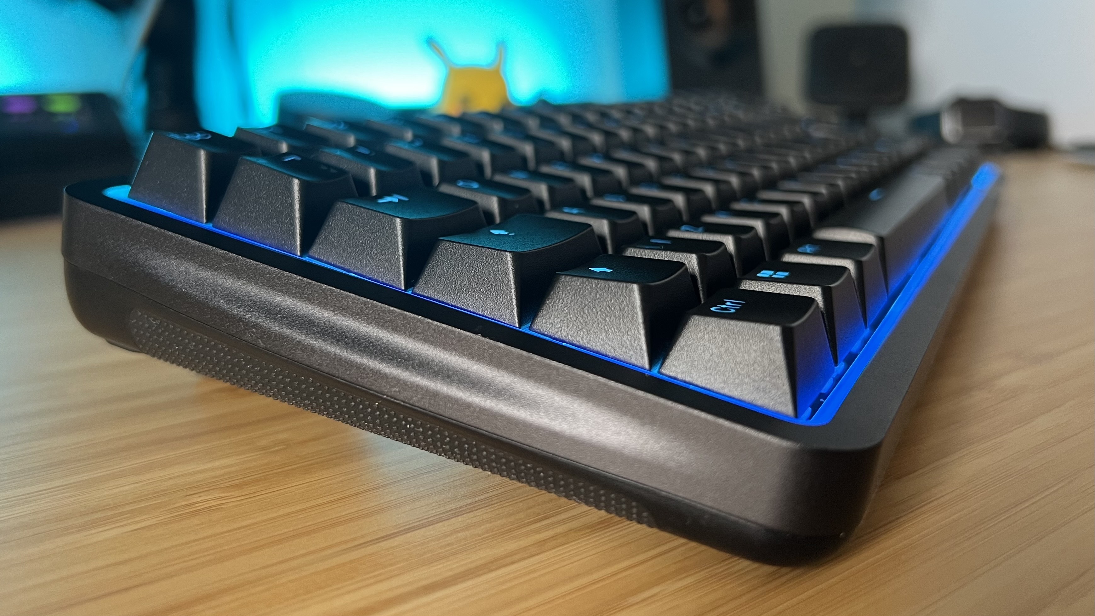 Side of NZXT Function Elite MiniTKL keyboard on a wooden desk, with plastic underside visible