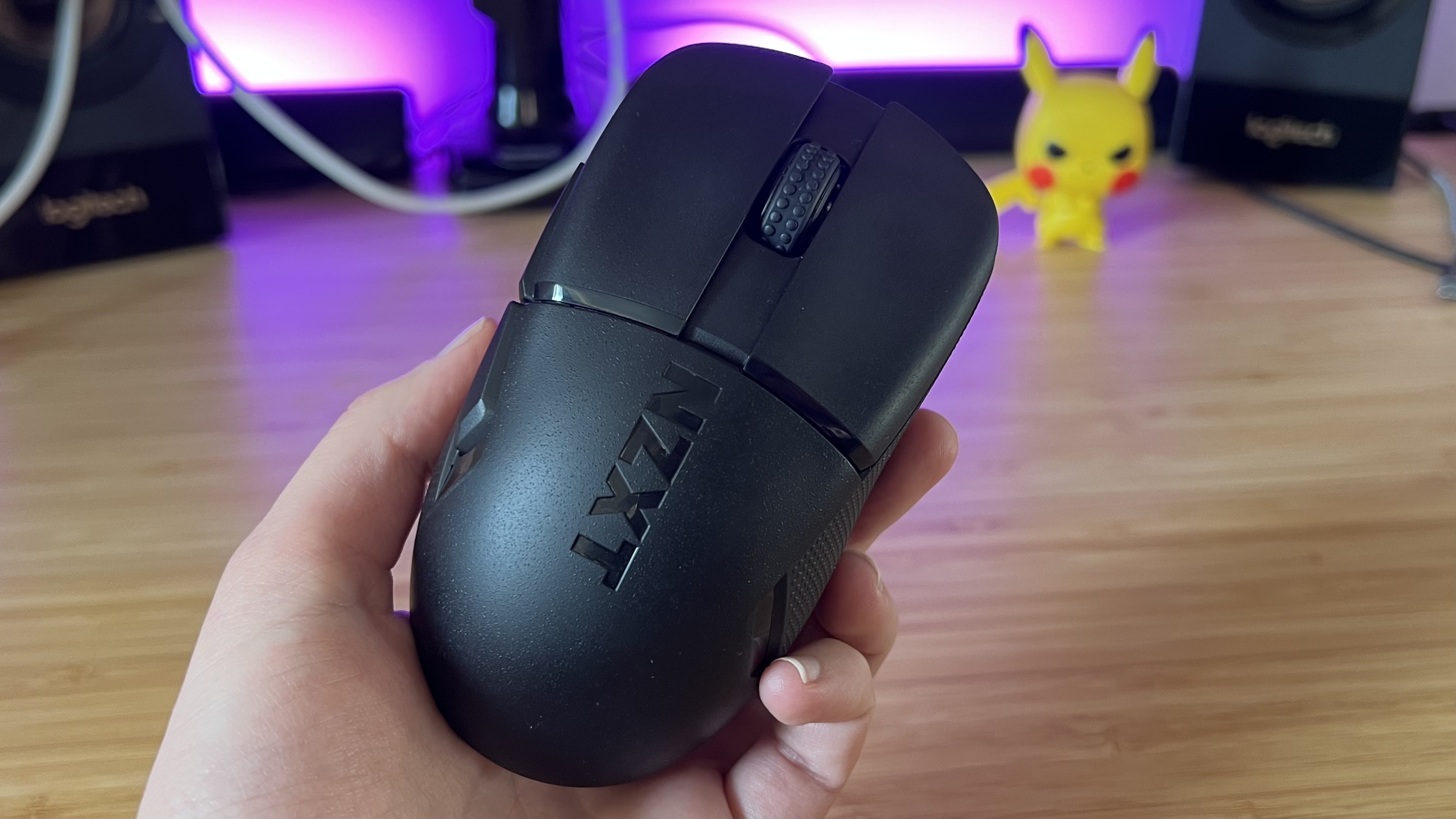 Hand holding NZXT Lift Elite Wireless gaming mouse against a PC setup