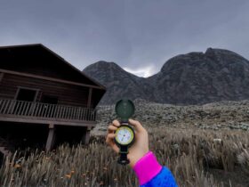 A hand holding a compass in front of a wooden cabin