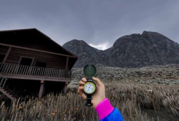 A hand holding a compass in front of a wooden cabin