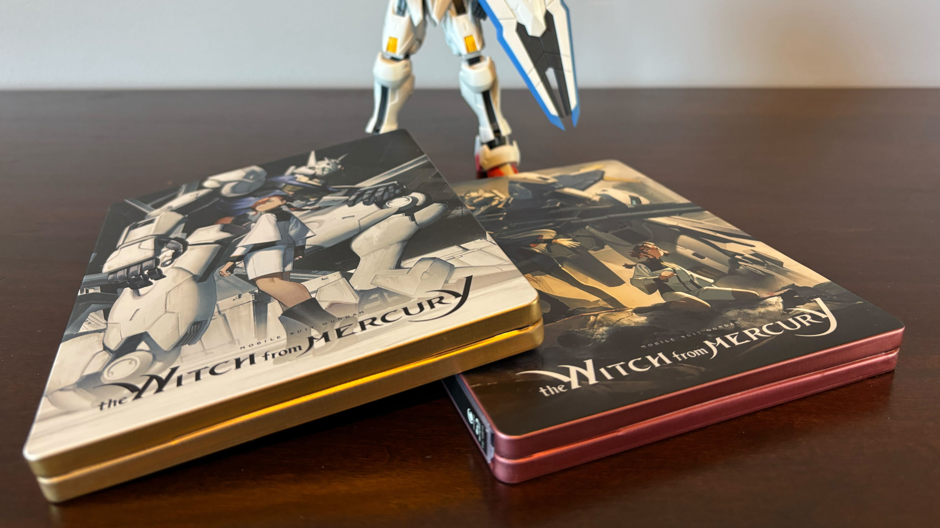 Mobile Suit Gundam: The Witch From Mercury steelbooks in front of an action figure, all on a wooden table