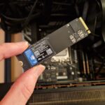 The WD Blue SN5000 4TB SSD being held above a gaming PC by a reviewer