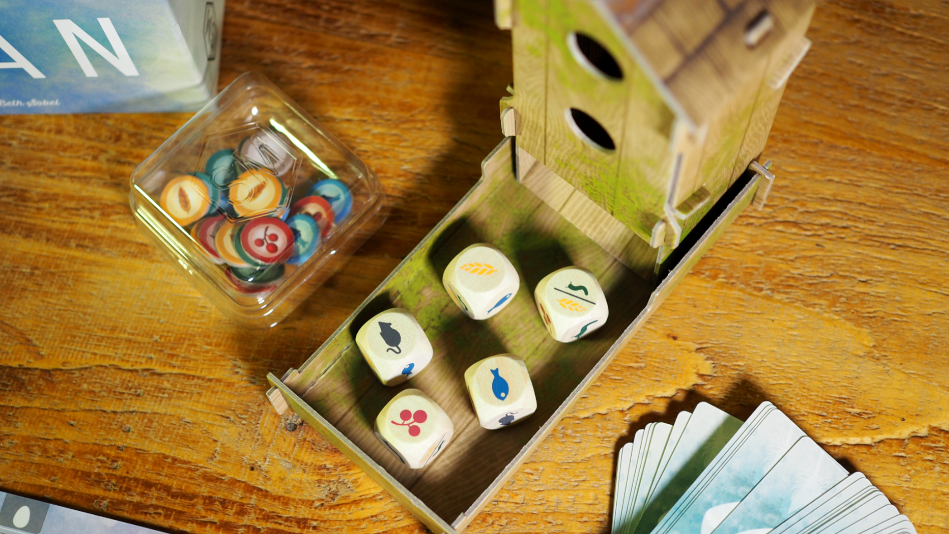 A top-down view of the dice tower, dice, tokens, and cards on a wooden table