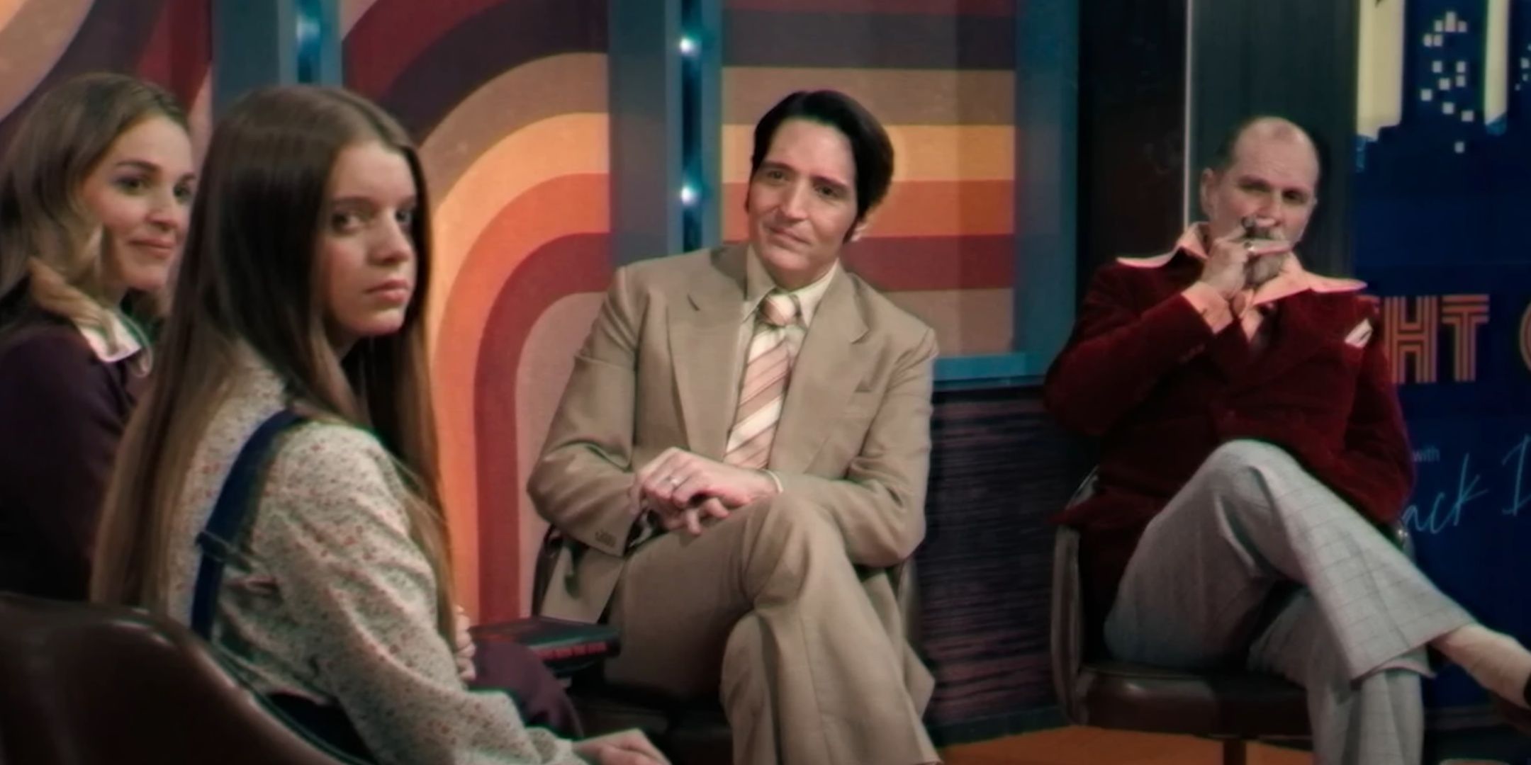 Jack Delroy surrounded by his talk show guests, as Lilly looks into the camera.