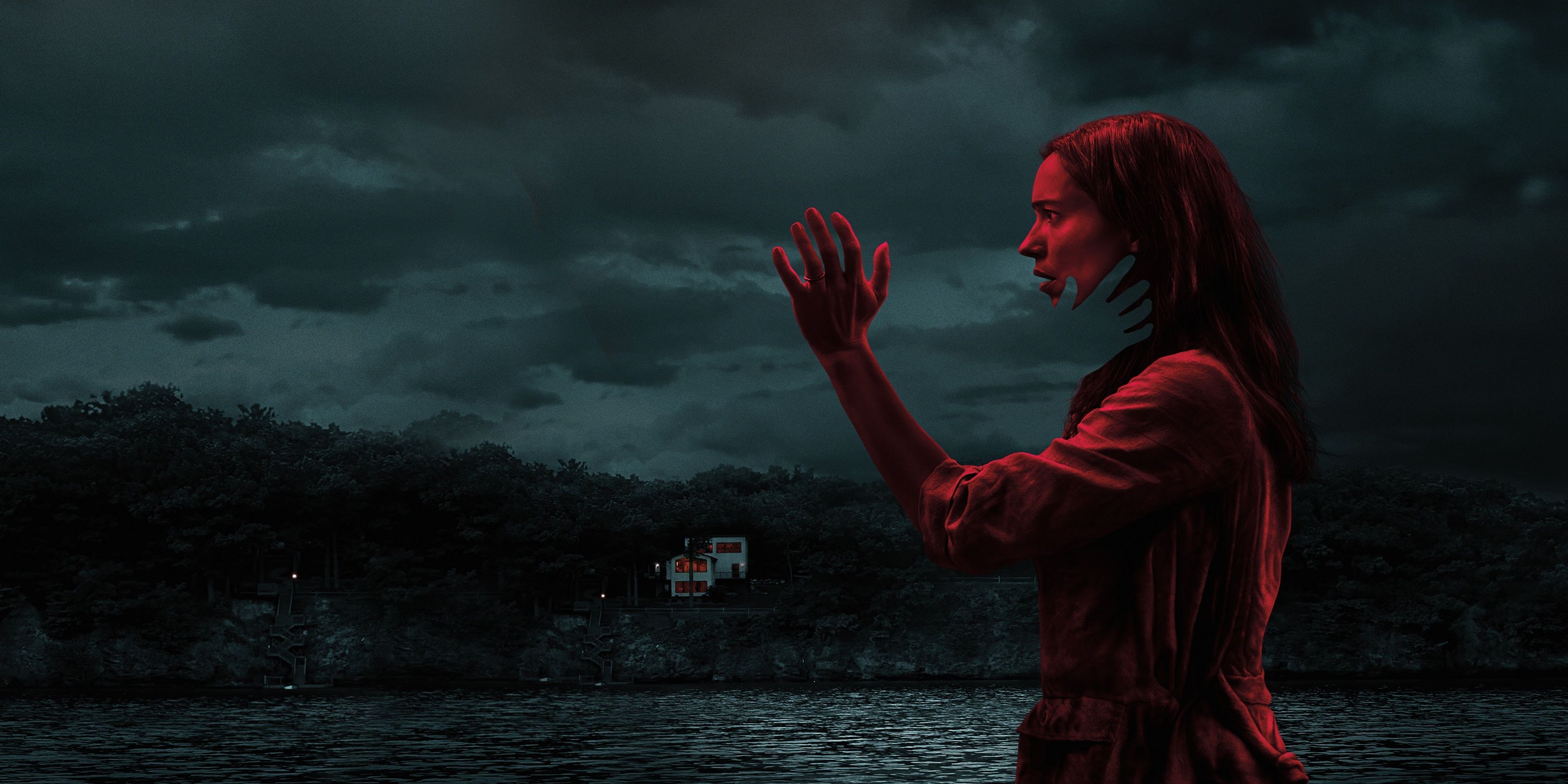Rebecca Hall's character Beth highlighted in red lighting as an invisible hand reaches out to touch her face and her home seen in the background on the main art for The Night House.