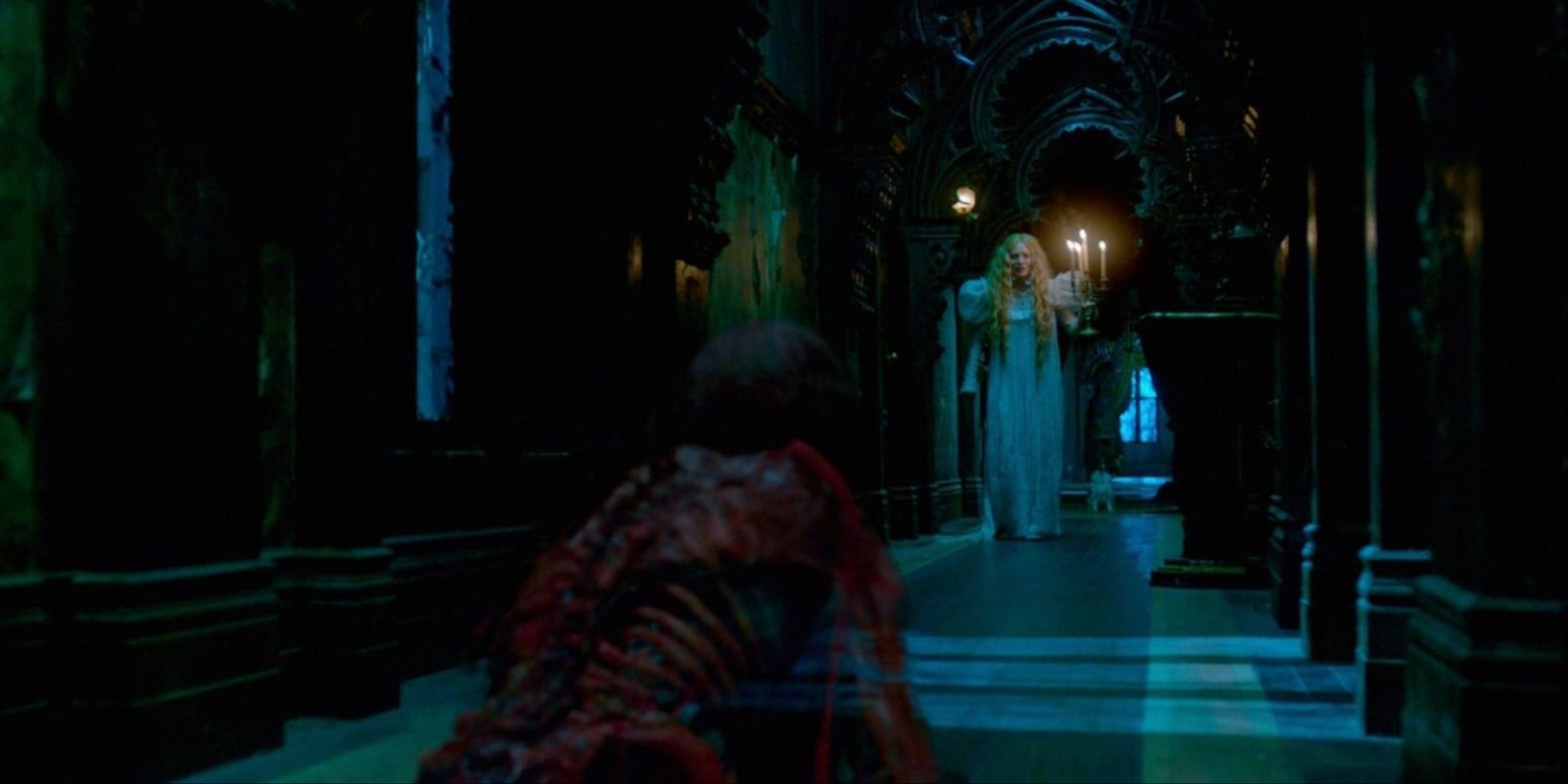 Mia Wasikowska's Edith Cushing holding a large candelabra walking down a dark hallway as a creepy red ghost crawls toward her on the ground in Crimson Peak.