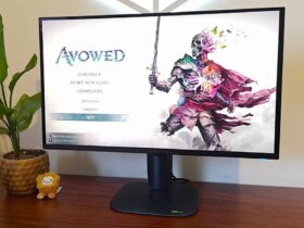 Alienware AW2725Q monitor on woodgrain desk next to plant with Avowed main menu on screen