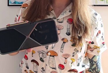 GamesRadar+ Hardware Editor Phil Hayton holding an RTX 5070 Founders Edition graphics card wearing a mushroom pattern shirt with a white wall in background.