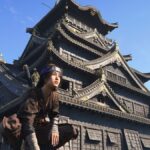 Naoe perched in front of a castle in Assassin's Creed Shadows