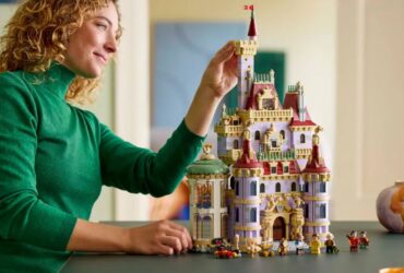 A woman places a brick onto the Lego Beauty and the Beast Castle, which sits on a dark table