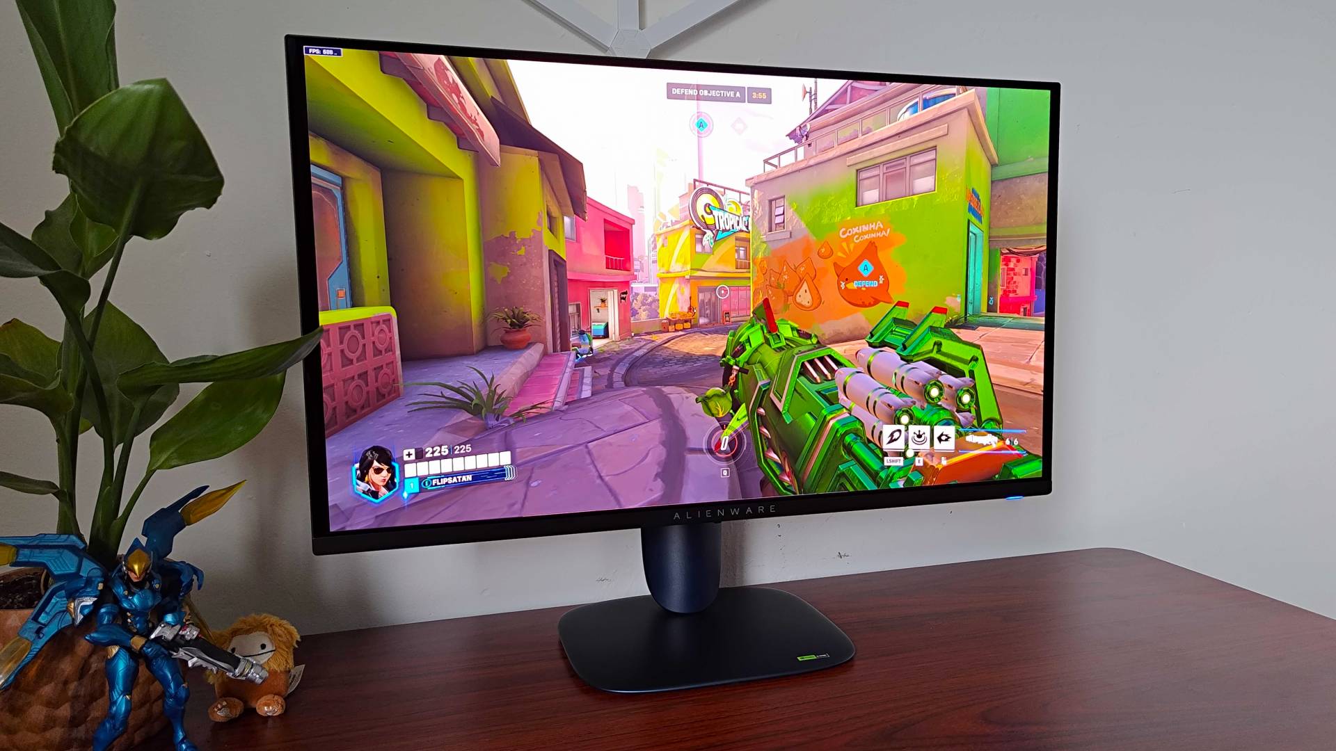 Alienware AW2725Q gaming monitor with Overwatch 2 gameplay on screen featuring Pharah holding green rocket launcher.