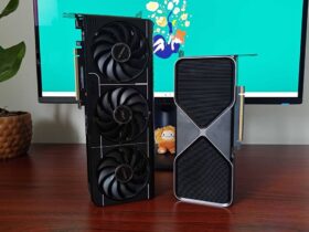 RTX 5070 Founders Edition and Asus Prime OC graphics card standing vertical on woodgrain desk next to plant and monitor