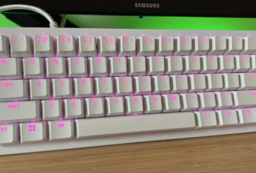 White Razer Huntsman V3 Pro Mini gaming keyboard on a wooden desk with green back lighting