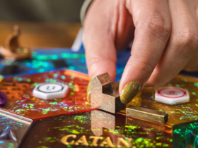 Sparkly Catan Hex tiles and metal buildings with a hand reaching down to move them