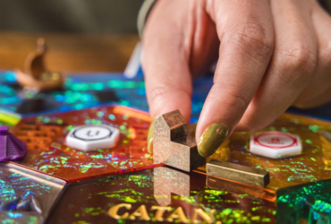 Sparkly Catan Hex tiles and metal buildings with a hand reaching down to move them