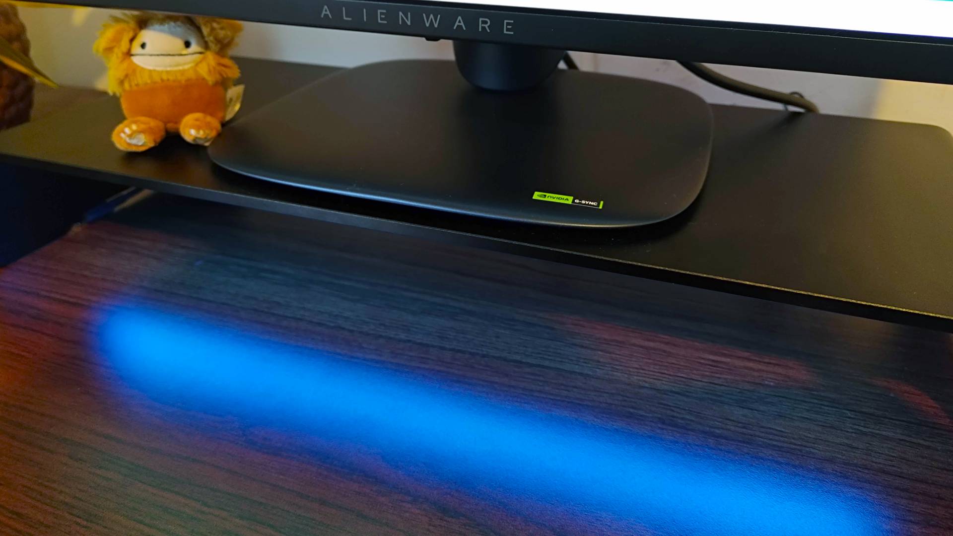 Close up of Razer Monitor Stand Chroma with blue light reflecting off desk and Alienware monitor pedestal on top.