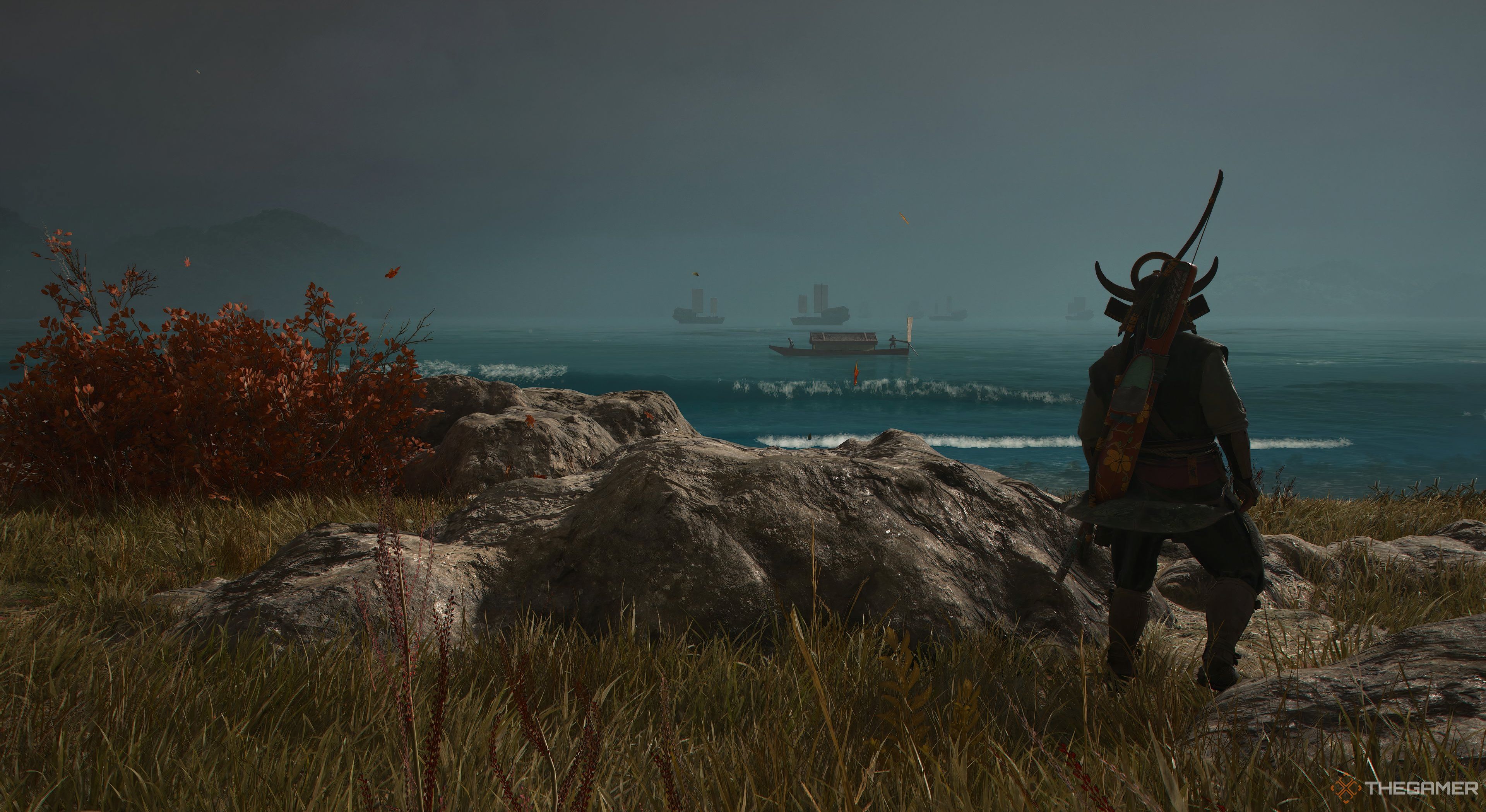 Assassins Creed Shadows Yaskue looking onwards at the boats. There are waves crashing towards him. A rock and a red bush are located beside him on the left.
