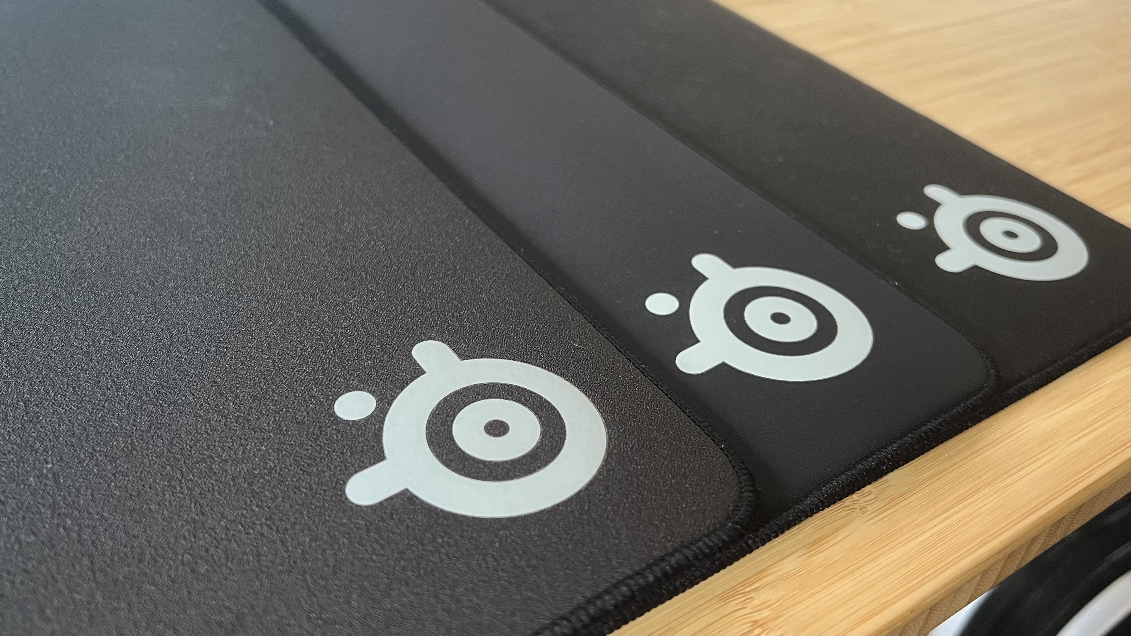 SteelSeries QcK Performance gaming mouse pad line on a wooden desk, with focus on brand logo