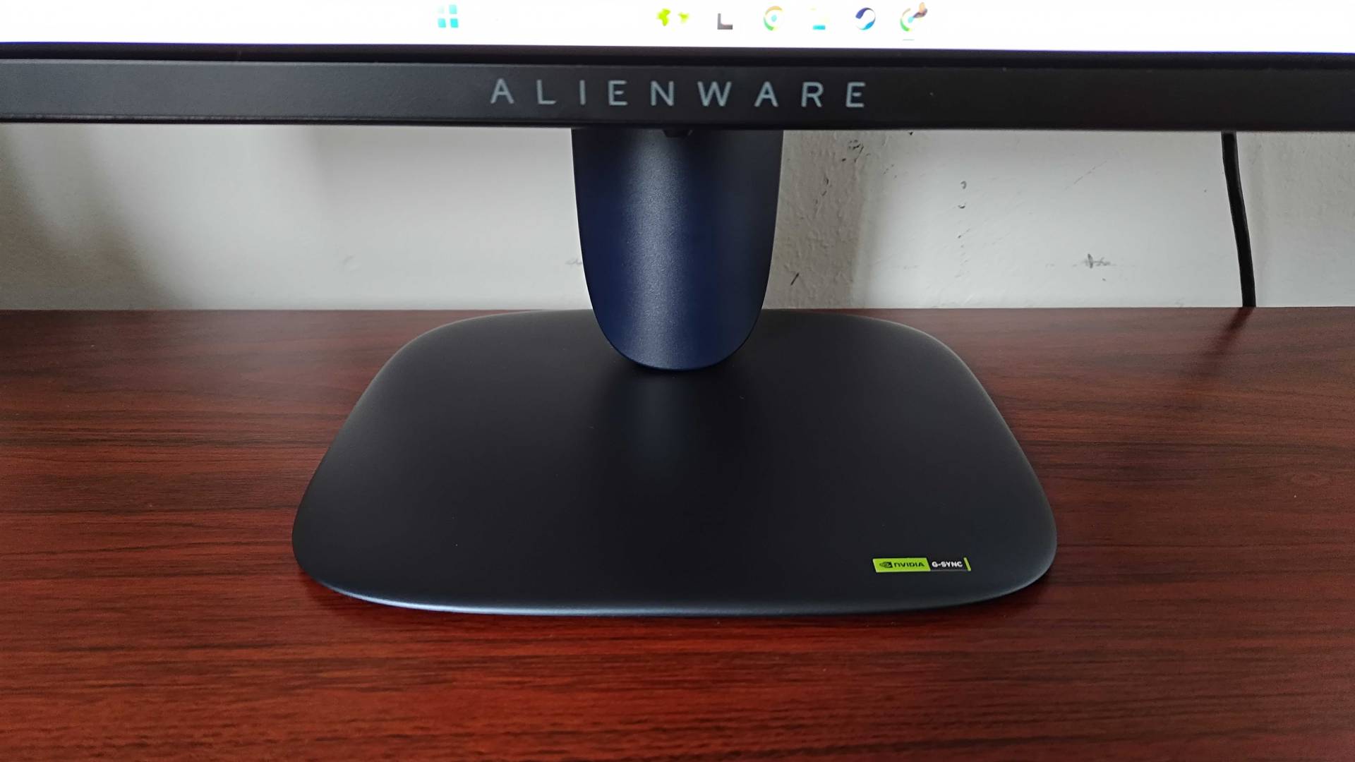 Close up  of Alienware AW2725Q gaming monitor stand sitting on woodgrain desk.