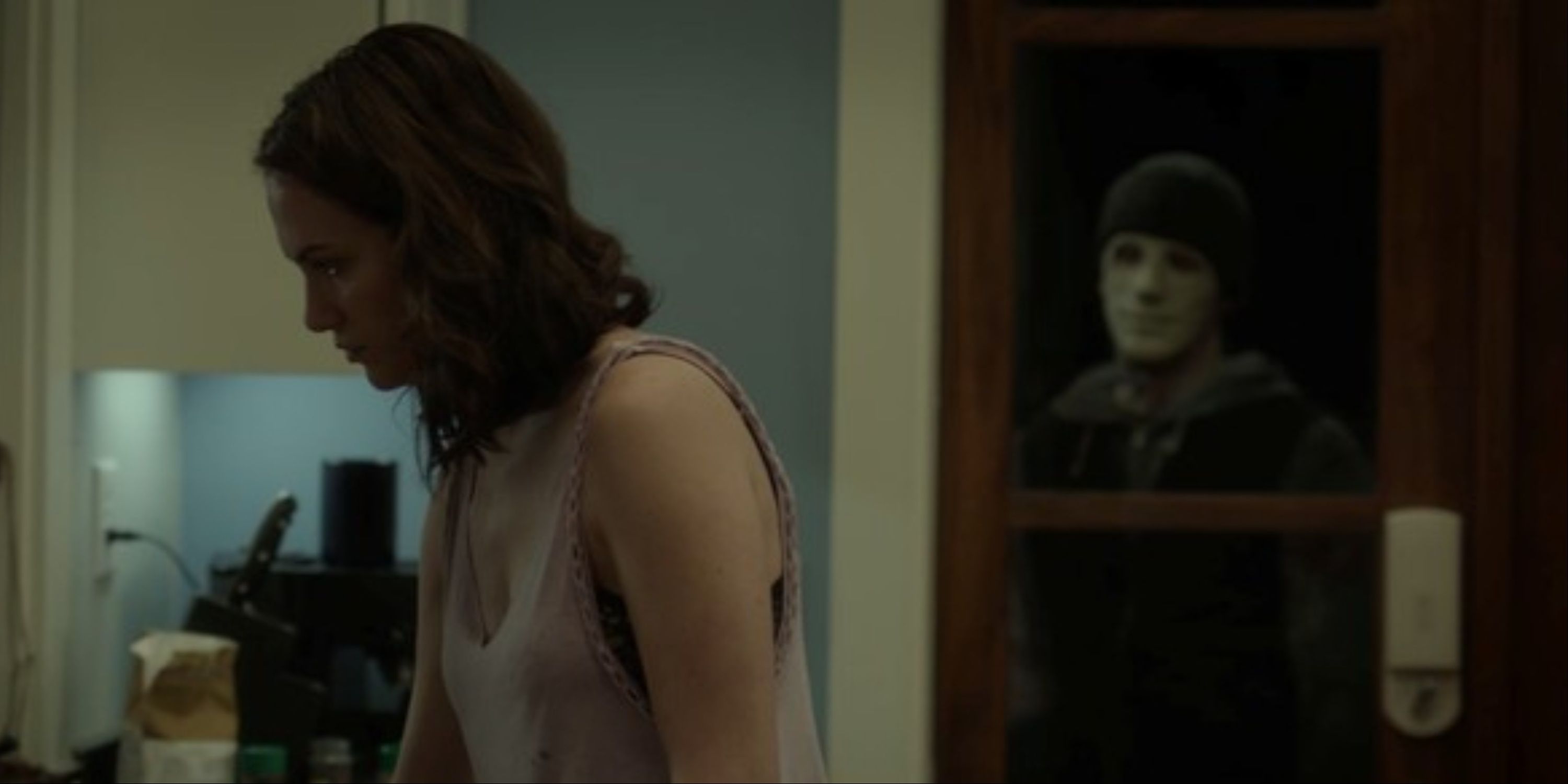 Kate Siegel in Hush with the masked intruder standing on the other side of the door and watching her.