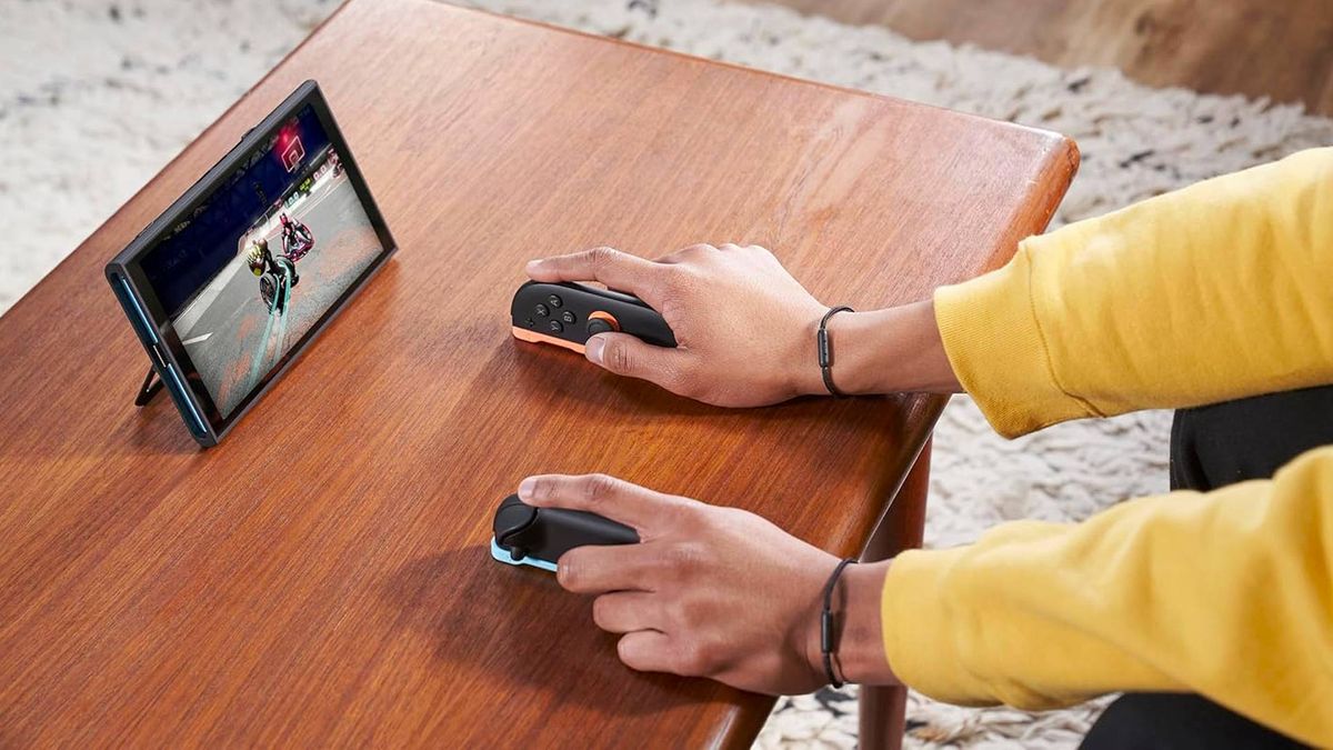 Player wearing yellow sweater using Nintendo Switch 2 JoyCon in mouse mode playing Drag x Drive on woodgrain coffee table.