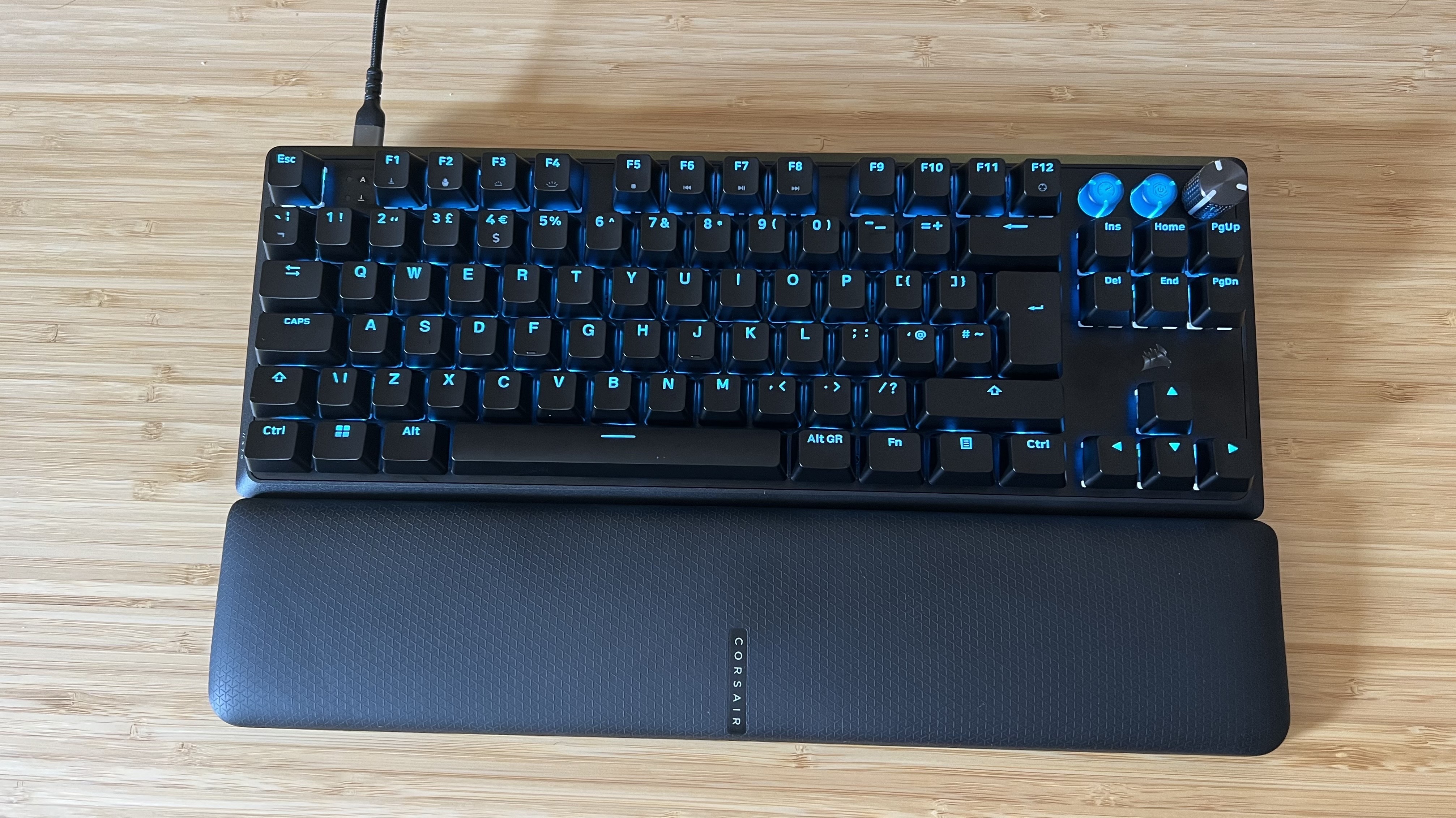 Corsair K70 Pro TKL gaming keyboard on a wooden desk with blue RGB lighting