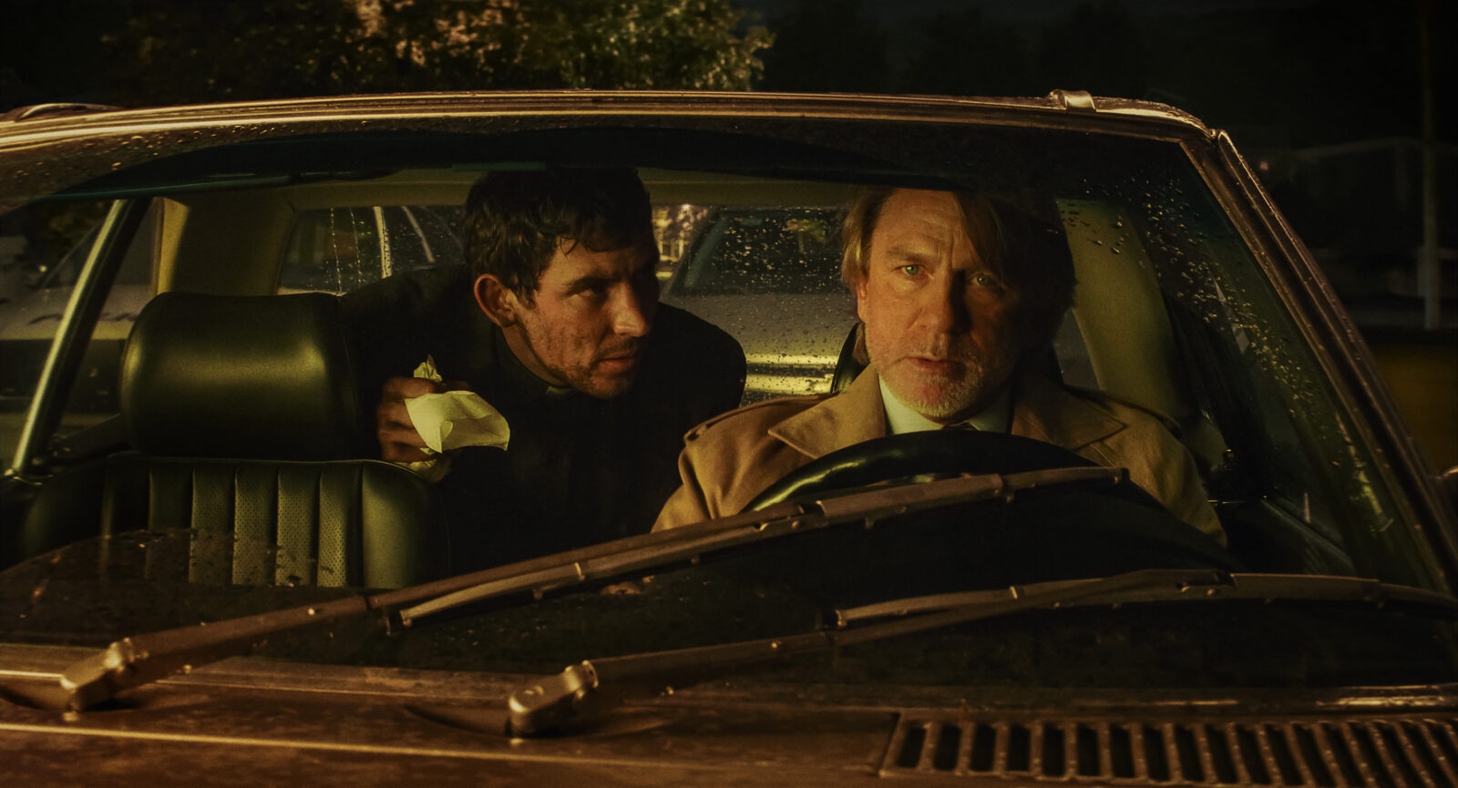 Father Jud in the back seat of Benoit Blanc's car talking to Benoit