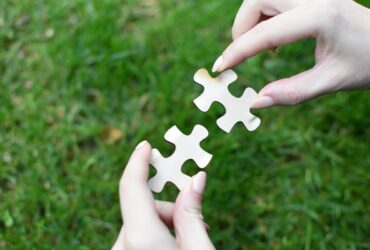 Two pieces of a jigsaw against a green background being pieced together.